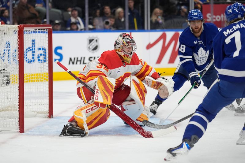 Oct 28, 2025; Toronto, Ontario, CAN; Calgary Flames goaltender Dustin Wolf (32) defends the goal as Toronto Maple Leafs forward William Nylander (88) and forward Bobby McMann (74) close in during the first period at Scotiabank Arena. Mandatory Credit: John E. Sokolowski-Imagn Images