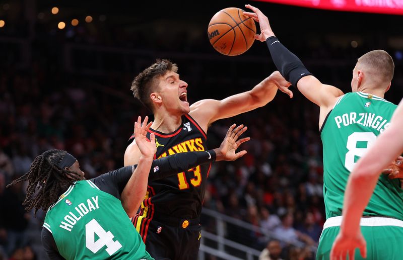 ATLANTA, GEORGIA - MARCH 28:  Bogdan Bogdanovic #13 of the Atlanta Hawks draws a foul as he drives against Jrue Holiday #4 and Kristaps Porzingis #8 of the Boston Celtics during the fourth quarter at State Farm Arena on March 28, 2024 in Atlanta, Georgia.  NOTE TO USER: User expressly acknowledges and agrees that, by downloading and/or using this photograph, user is consenting to the terms and conditions of the Getty Images License Agreement.  (Photo by Kevin C. Cox/Getty Images)