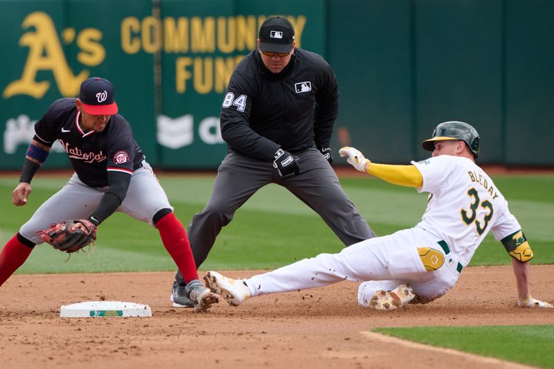Apr 14, 2024; Oakland, California, USA; Oakland Athletics outfielder JJ Bleday (33) slides against Washington Nationals second baseman Ildemaro Vargas (14) and umpire John Libka (84) watches the play during the first inning at Oakland-Alameda County Coliseum. Mandatory Credit: Robert Edwards-USA TODAY Sports