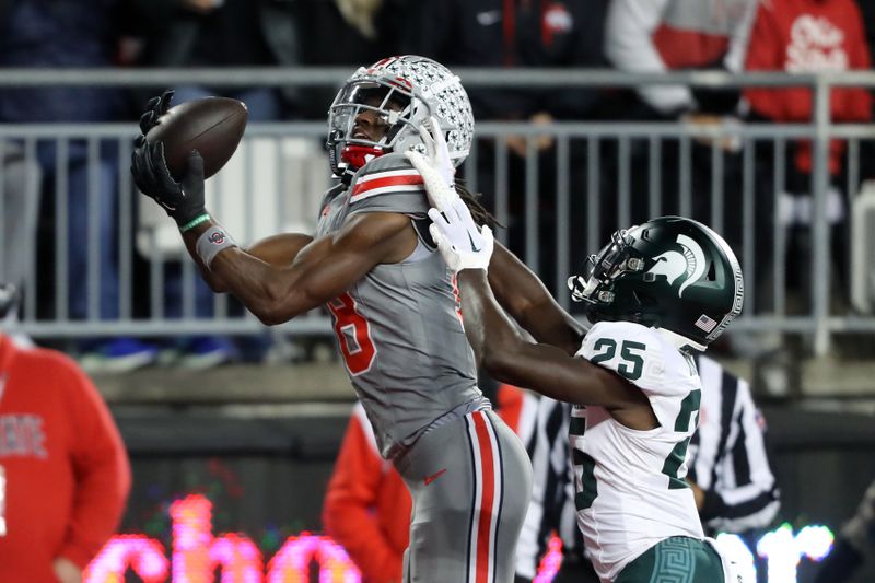 Nov 11, 2023; Columbus, Ohio, USA;  Ohio State Buckeyes wide receiver Marvin Harrison Jr. (18) scores a touchdown as Michigan State Spartans defensive back Chance Rucker (25) defends during the first quarter at Ohio Stadium. Mandatory Credit: Joseph Maiorana-USA TODAY Sports