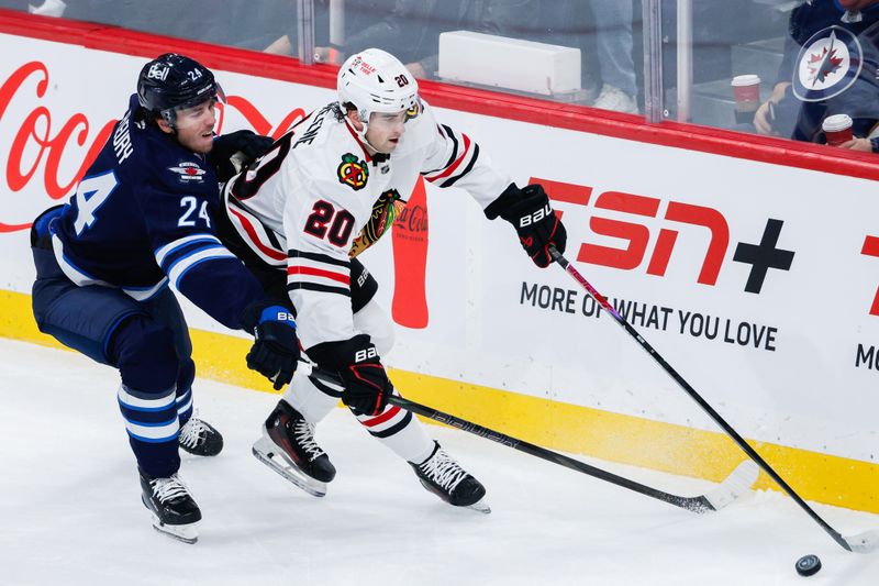 Oct 30, 2025; Winnipeg, Manitoba, CAN;  Chicago Blackhawks forward Ryan Greene (20) tries to skate away from Winnipeg Jets defenseman Hayden Fleury (24) during the first period at Canada Life Centre. Mandatory Credit: Terrence Lee-Imagn Images