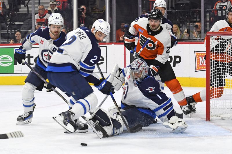 Mar 6, 2025; Philadelphia, Pennsylvania, USA; Winnipeg Jets defenseman Dylan DeMelo (2) looks to clear the puck after goaltender Eric Comrie (1) made a save against the Philadelphia Flyers during the first period at Wells Fargo Center. Mandatory Credit: Eric Hartline-Imagn Images