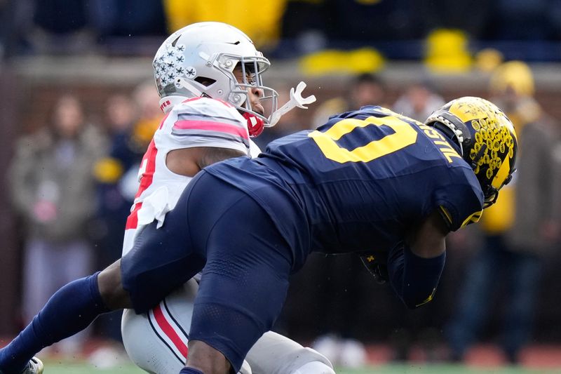 Nov 25, 2023; Ann Arbor, Michigan, USA; Michigan Wolverines defensive back Mike Sainristil (0) hits Ohio State Buckeyes running back TreVeyon Henderson (32) during the first half of the NCAA football game at Michigan Stadium. Mandatory Credit: Adam Cairns-USA TODAY Sports