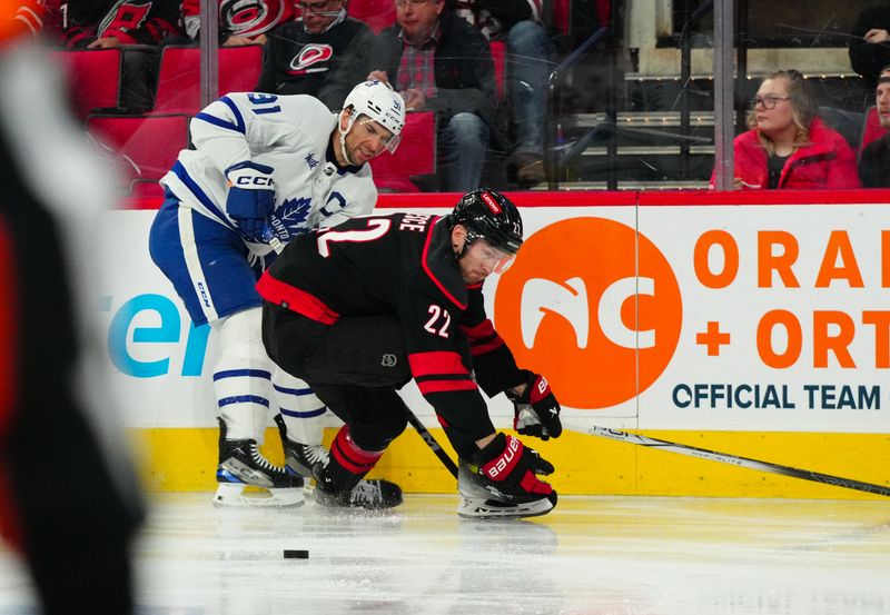 Mar 24, 2024; Raleigh, North Carolina, USA;  Toronto Maple Leafs center John Tavares (91) slips the puck past Carolina Hurricanes defenseman Brett Pesce (22) during the second period at PNC Arena. Mandatory Credit: James Guillory-USA TODAY Sports