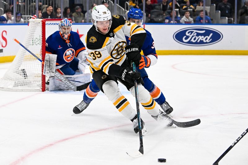 Nov 27, 2024; Elmont, New York, USA;  Boston Bruins center Morgan Geekie (39) controls the puck  defended by New York Islanders defenseman Isaiah George (36) during the first period at UBS Arena. Mandatory Credit: Dennis Schneidler-Imagn Images