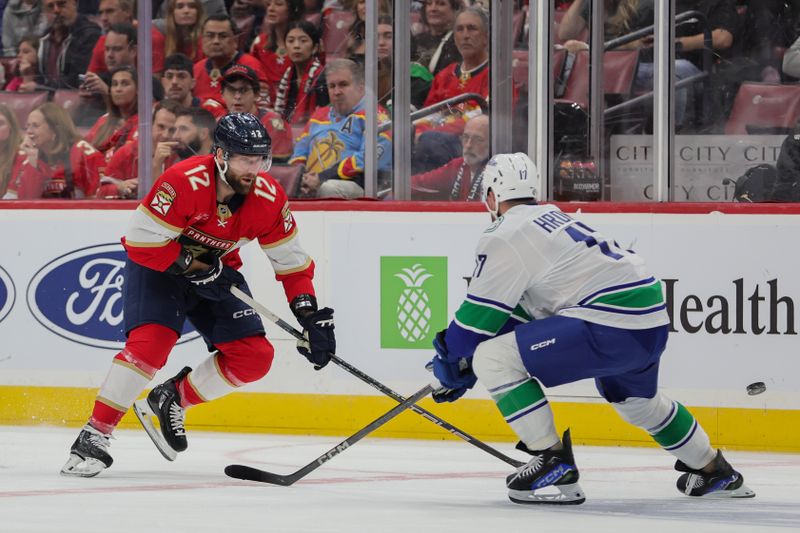 Oct 17, 2024; Sunrise, Florida, USA; Florida Panthers left wing Jonah Gadjovich (12) moves the puck past Vancouver Canucks defenseman Filip Hronek (17) during the first period at Amerant Bank Arena. Mandatory Credit: Sam Navarro-Imagn Images