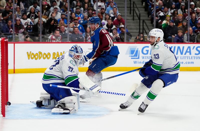 Dec 2, 2025; Denver, Colorado, USA; Colorado Avalanche center Brock Nelson (11) scores on Vancouver Canucks goaltender Kevin Lankinen (32) as center Teddy Blueger (53) defends in the second period at Ball Arena. Mandatory Credit: Ron Chenoy-Imagn Images