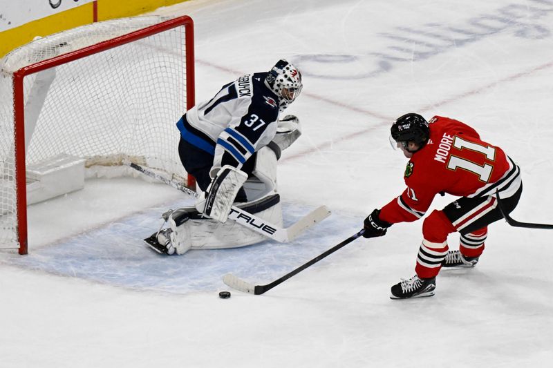 Jan 19, 2026; Chicago, Illinois, USA;  Chicago Blackhawks center Oliver Moore (11) shoots the puck against Winnipeg Jets goaltender Connor Hellebuyck (37) during the first period at United Center. Mandatory Credit: Matt Marton-Imagn Images