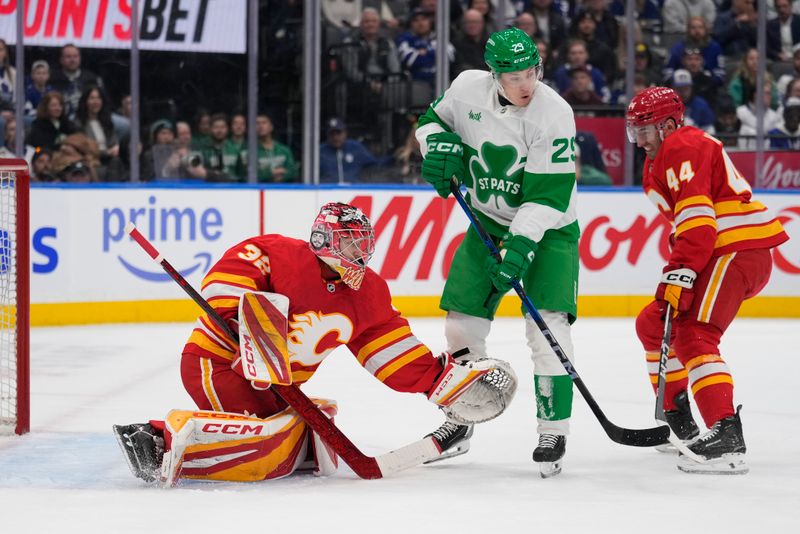 Mar 17, 2025; Toronto, Ontario, CAN; Calgary Flames goaltender Dustin Wolf (32) makes a save as Toronto Maple Leafs forward Pontus Holmberg (29) tries to deflect the puck during the first period at Scotiabank Arena. Mandatory Credit: John E. Sokolowski-Imagn Images