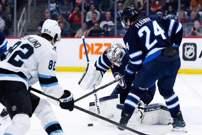Jan 24, 2025; Winnipeg, Manitoba, CAN; Winnipeg Jets goalie Connor Hellebuyck (37) makes a save as Utah Hockey Club forward Kevin Stenlund (82) and Winnipeg Jets defenseman Hayden Fleury (24) look for a rebound during the first period at Canada Life Centre. Mandatory Credit: Terrence Lee-Imagn Images