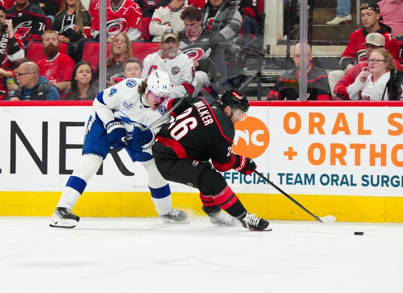 Oct 11, 2024; Raleigh, North Carolina, USA;  Tampa Bay Lightning center Conor Geekie (14) battles for the puck against  Carolina Hurricanes defenseman Sean Walker (26) during the second period at PNC Arena. Mandatory Credit: James Guillory-Imagn Images