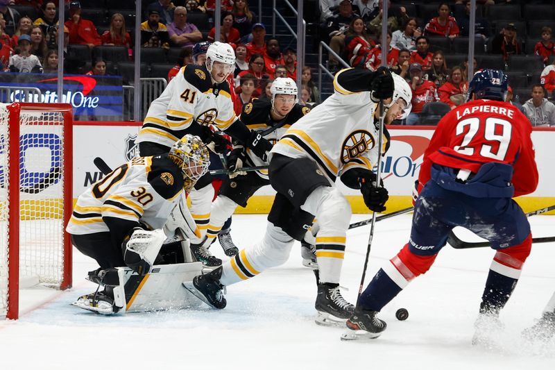 Oct 5, 2024; Washington, District of Columbia, USA; Boston Bruins center John Beecher (19) clears the puck from Washington Capitals center Hendrix Lapierre (29) in front of Bruins goaltender Brandon Bussi (30) in the third period at Capital One Arena. Mandatory Credit: Geoff Burke-Imagn Images