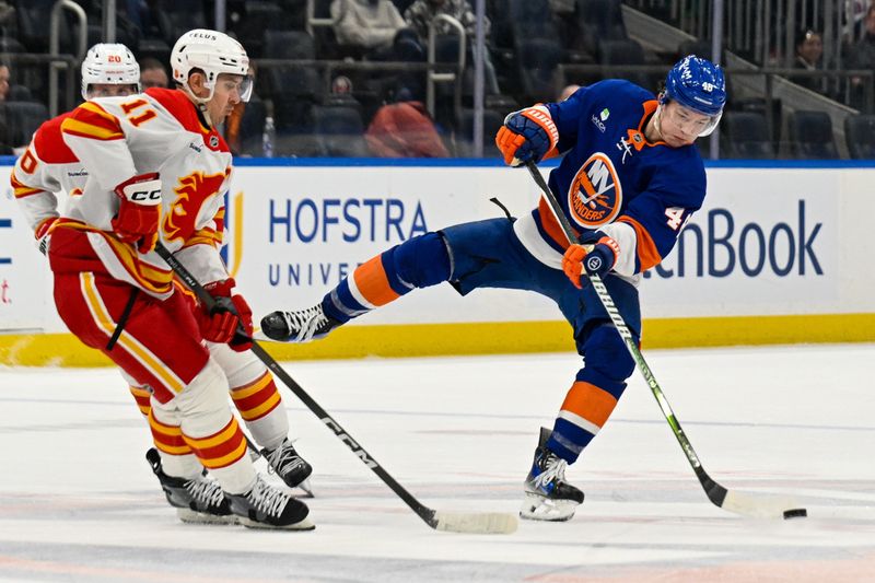 Mar 14, 2026; Elmont, New York, USA;  New York Islanders defenseman Matthew Schaefer (48) plays the puck into the zone defended by Calgary Flames center Mikael Backlund (11) during the second period at UBS Arena. Mandatory Credit: Dennis Schneidler-Imagn Images