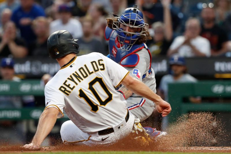 May 22, 2023; Pittsburgh, Pennsylvania, USA;  Pittsburgh Pirates left fielder Bryan Reynolds (10) slides home safely to score a run ahead of the tag of Texas Rangers catcher Jonah Heim (28) during the seventh inning at PNC Park. Mandatory Credit: Charles LeClaire-USA TODAY Sports