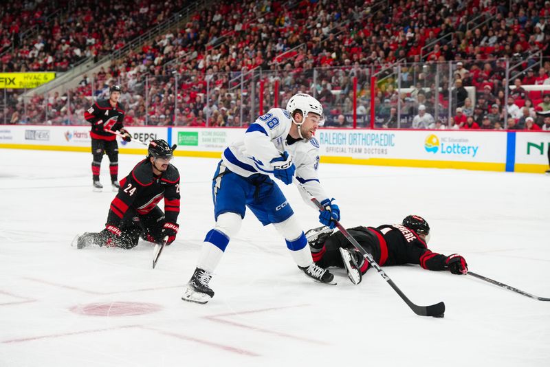 Mar 11, 2025; Raleigh, North Carolina, USA;  Carolina Hurricanes center Seth Jarvis (24) and defenseman Shayne Gostisbehere (4) try to break up the play against Tampa Bay Lightning left wing Brandon Hagel (38) during the second period at Lenovo Center. Mandatory Credit: James Guillory-Imagn Images