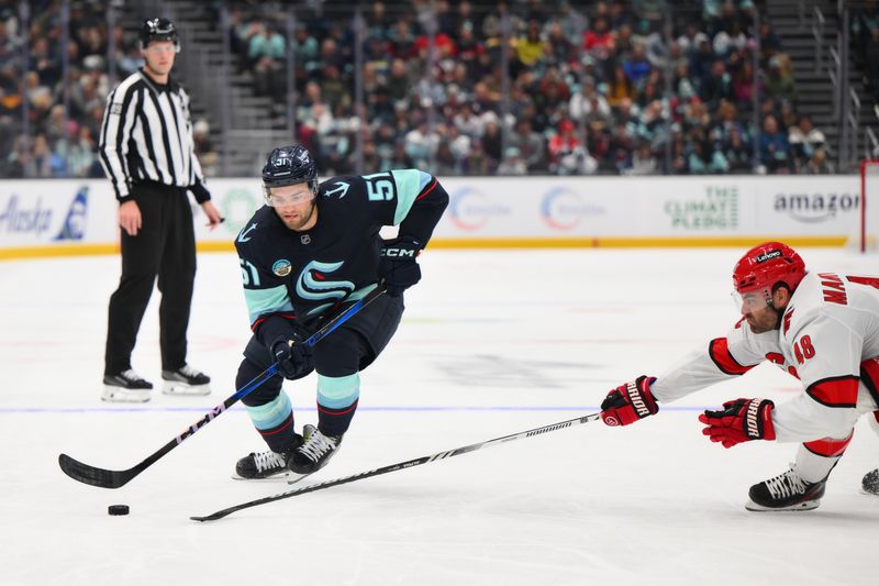 Oct 26, 2024; Seattle, Washington, USA; Seattle Kraken center Shane Wright (51) advances the puck while defended by Carolina Hurricanes left wing Jordan Martinook (48) during the first period at Climate Pledge Arena. Mandatory Credit: Steven Bisig-Imagn Images