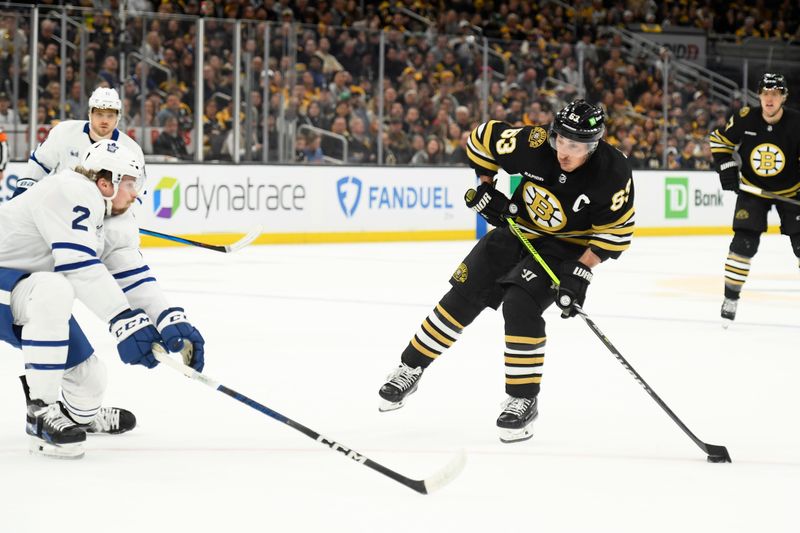 Apr 20, 2024; Boston, Massachusetts, USA;Boston Bruins left wing Brad Marchand (63) shoots the puck while Toronto Maple Leafs defenseman Simon Benoit (2) defends during the first period in game one of the first round of the 2024 Stanley Cup Playoffs at TD Garden. Mandatory Credit: Bob DeChiara-USA TODAY Sports