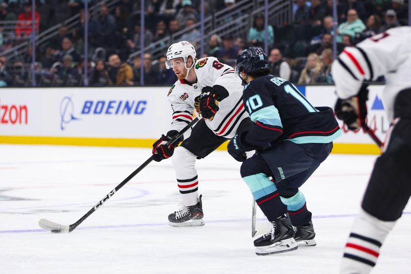 Nov 3, 2025; Seattle, Washington, USA; Chicago Blackhawks defenseman Sam Rinzel (6) passes the puck past Seattle Kraken center Matty Beniers (10) in the first period at Climate Pledge Arena. Mandatory Credit: Kevin Ng-Imagn Images