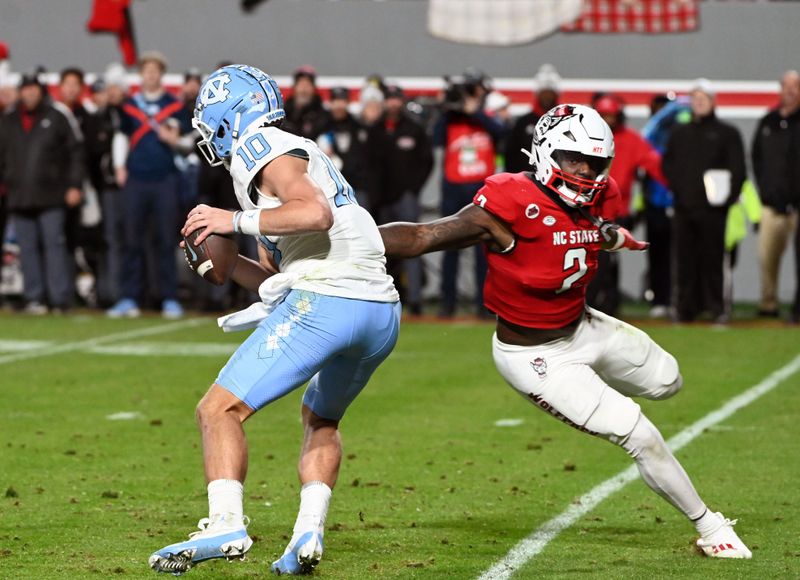 Nov 25, 2023; Raleigh, North Carolina, USA; North Carolina Tar Heels quarterback Drake Maye (10) is pressured by North Carolina State Wolfpack linebacker Jaylon Scott (2) during the first half at Carter-Finley Stadium. Mandatory Credit: Rob Kinnan-USA TODAY Sports