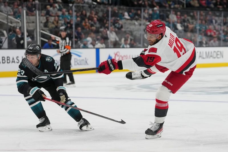 Oct 14, 2025; San Jose, California, USA;  Carolina Hurricanes defenseman K'Andre Miller (19) shoots the puck during the second period against San Jose Sharks center Barclay Goodrow (23) at SAP Center at San Jose. Mandatory Credit: Stan Szeto-Imagn Images