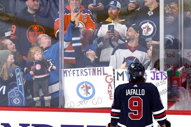 Mar 26, 2024; Winnipeg, Manitoba, CAN; Winnipeg Jets left wing Alex Iafallo (9) tosses a puck to fans before a game against the Edmonton Oilers at Canada Life Centre. Mandatory Credit: James Carey Lauder-USA TODAY Sports