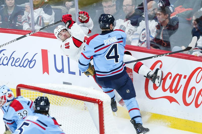 Dec 4, 2023; Winnipeg, Manitoba, CAN; Winnipeg Jets defenseman Neal Pionk (4) boards Carolina Hurricanes forward Jordan Martinook (48) during the third period at Canada Life Centre. Mandatory Credit: Terrence Lee-USA TODAY Sports