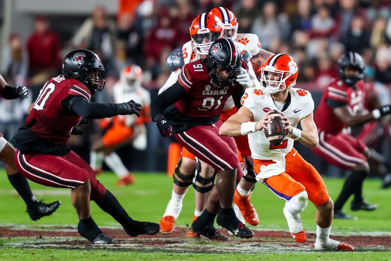 Nov 25, 2023; Columbia, South Carolina, USA; Clemson Tigers quarterback Cade Klubnik (2) scrambles under pressure from South Carolina Gamecocks defensive tackle T.J. Sanders (90) and defensive tackle Tonka Hemingway (91) in the first quarter at Williams-Brice Stadium. Mandatory Credit: Jeff Blake-USA TODAY Sports