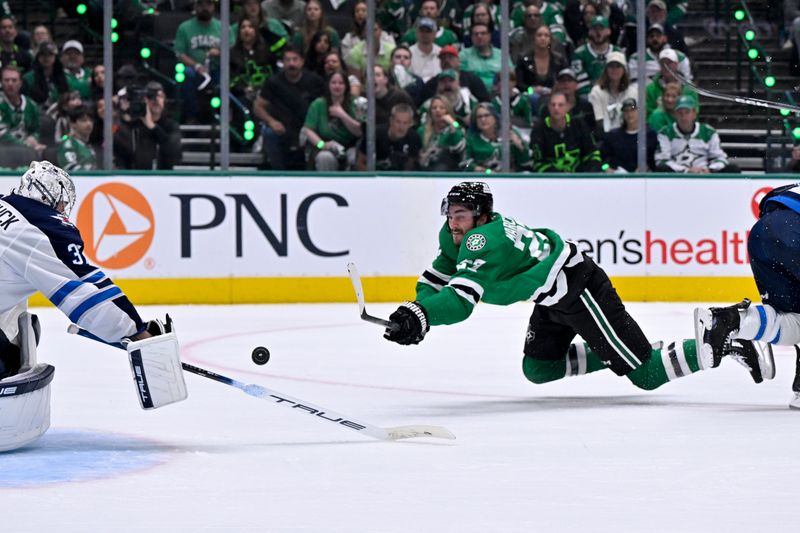 May 11, 2025; Dallas, Texas, USA; Dallas Stars left wing Mason Marchment (27) is tripped up as he shoots the puck towards Winnipeg Jets goaltender Connor Hellebuyck (37) during the second period in game three of the second round of the 2025 Stanley Cup Playoffs at American Airlines Center. Mandatory Credit: Jerome Miron-Imagn Images