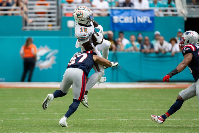 Miami Dolphins wide receiver Tyreek Hill (10) jumps in the air to catch a pass and hit by New England Patriots defensive back Myles Bryant (27) during an NFL football game, Sunday, Oct. 29, 2023, in Miami Gardens, Fla. (AP Photo/Doug Murray)