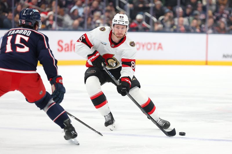 Dec 11, 2025; Columbus, Ohio, USA; Ottawa Senators defenseman Jake Sanderson (85) controls the puck as Columbus Blue Jackets defenseman Dante Fabbro (15) defends during the first period at Nationwide Arena. Mandatory Credit: Joseph Maiorana-Imagn Images