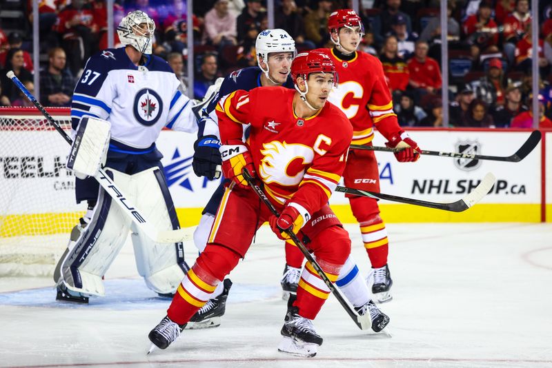 Oct 4, 2024; Calgary, Alberta, CAN; Calgary Flames center Mikael Backlund (11) and Winnipeg Jets goaltender Connor Hellebuyck (37) fights for position in front of Winnipeg Jets goaltender Connor Hellebuyck (37) during the second period at Scotiabank Saddledome. Mandatory Credit: Sergei Belski-Imagn Images