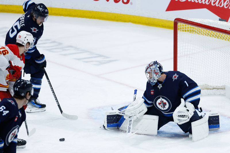 Jan 26, 2025; Winnipeg, Manitoba, CAN;  Winnipeg Jets goalie Eric Comrie (1) makes a save as Winnipeg Jets forward Mark Scheifele (55) and Calgary Flames forward Martin Pospisil (76) look for a rebound during the third period at Canada Life Centre. Mandatory Credit: Terrence Lee-Imagn Images