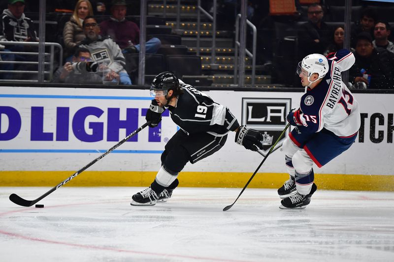 Mar 16, 2023; Los Angeles, California, USA; Los Angeles Kings left wing Alex Iafallo (19) moves the puck ahead of Columbus Blue Jackets defenseman Gavin Bayreuther (15) during the second period at Crypto.com Arena. Mandatory Credit: Gary A. Vasquez-USA TODAY Sports