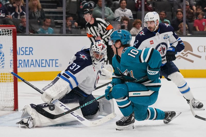 Nov 7, 2025; San Jose, California, USA;  Winnipeg Jets goalie Connor Hellebuyck (37) makes a save and defenseman Dylan DeMelo (2) watches the play against San Jose Sharks center Ty Dellandrea (10) during the second period at SAP Center at San Jose. Mandatory Credit: David Gonzales-Imagn Images