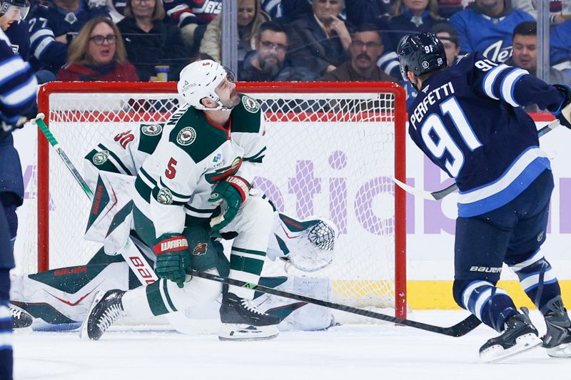 Nov 23, 2025; Winnipeg, Manitoba, CAN;  Minnesota Wild defenseman Jake Middleton (5) attempts to block a shot by Winnipeg Jets forward Cole Perfetti (91) during the first period at Canada Life Centre. Mandatory Credit: Terrence Lee-Imagn Images