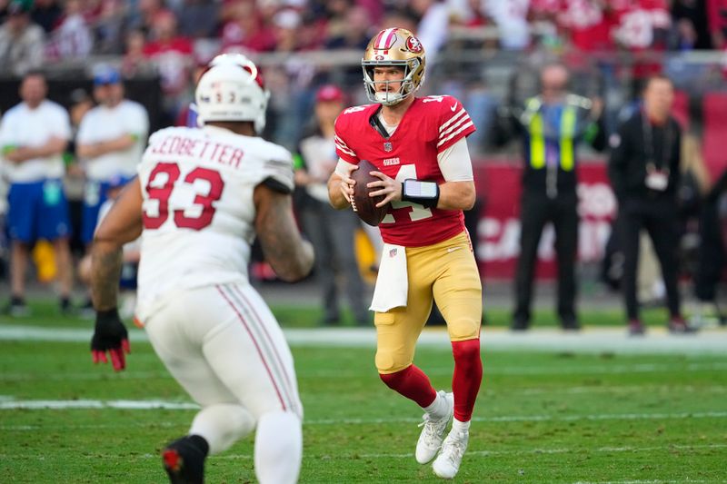 San Francisco 49ers quarterback Sam Darnold, right, looks to pass against Arizona Cardinals defensive end Jonathan Ledbetter (93) during the first half of an NFL football game Sunday, Dec. 17, 2023, in Glendale, Ariz. (AP Photo/Matt York)