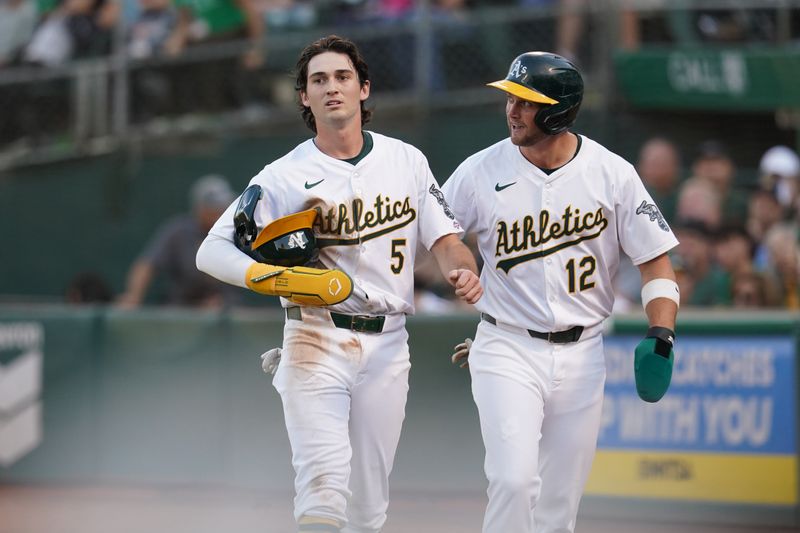 Jul 19, 2024; Oakland, California, USA; Oakland Athletics shortstop Jacob Wilson (5) and third baseman Max Schuemann (12) walk towards the dugout after scoring runs against the Los Angeles Angels in the third inning at Oakland-Alameda County Coliseum. Mandatory Credit: Cary Edmondson-USA TODAY Sports