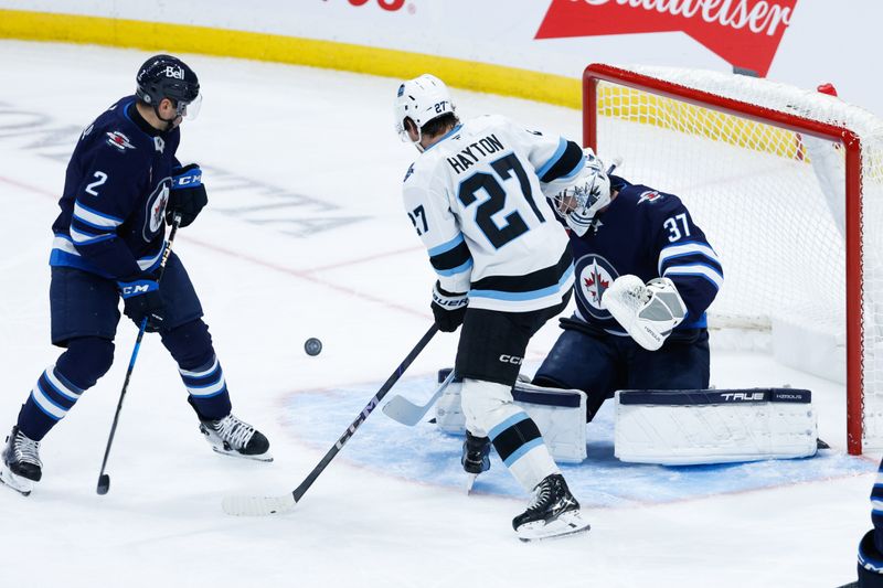 Nov 5, 2024; Winnipeg, Manitoba, CAN;  Winnipeg Jets goalie Connor Hellebuyck (37) makes a save as Utah Hockey Club forward Barrett Hayton (27) and Winnipeg Jets defenseman Dylan DeMelo (2) look for the puck during the third period at Canada Life Centre. Mandatory Credit: Terrence Lee-Imagn Images