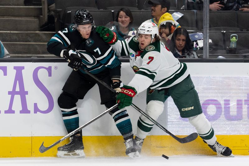 Nov 7, 2024; San Jose, California, USA;  San Jose Sharks center Nico Sturm (7) and Minnesota Wild defenseman Brock Faber (7) fight for control of the puck during the first period at SAP Center at San Jose. Mandatory Credit: Stan Szeto-Imagn Images