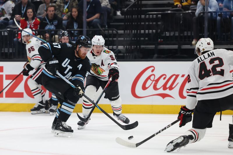 Feb 25, 2025; Salt Lake City, Utah, USA; Utah Hockey Club left wing Lawson Crouse (67) passes the puck against Chicago Blackhawks defenseman Connor Murphy (5) and defenseman Nolan Allan (42) during the second period at Delta Center. Mandatory Credit: Rob Gray-Imagn Images