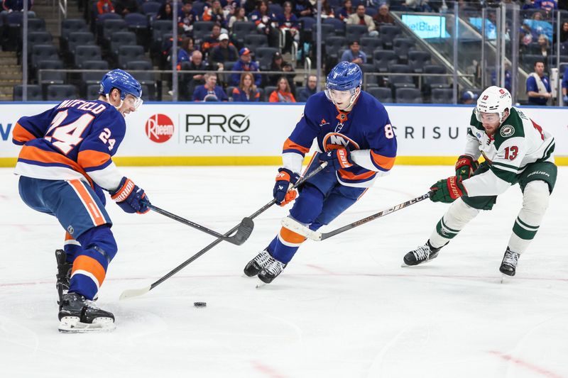 Apr 4, 2025; Elmont, New York, USA;  New York Islanders defenseman Scott Mayfield (24) and Noah Dobson (8) battle for control of the puck with Minnesota Wild center Yakov Trenin (13) in the third period at UBS Arena. Mandatory Credit: Wendell Cruz-Imagn Images