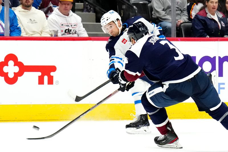 Dec 7, 2023; Denver, Colorado, USA; Winnipeg Jets defenseman Neal Pionk (4) shoots the puck past Colorado Avalanche defenseman Jack Johnson (3) in the first period at Ball Arena. Mandatory Credit: Ron Chenoy-USA TODAY Sports