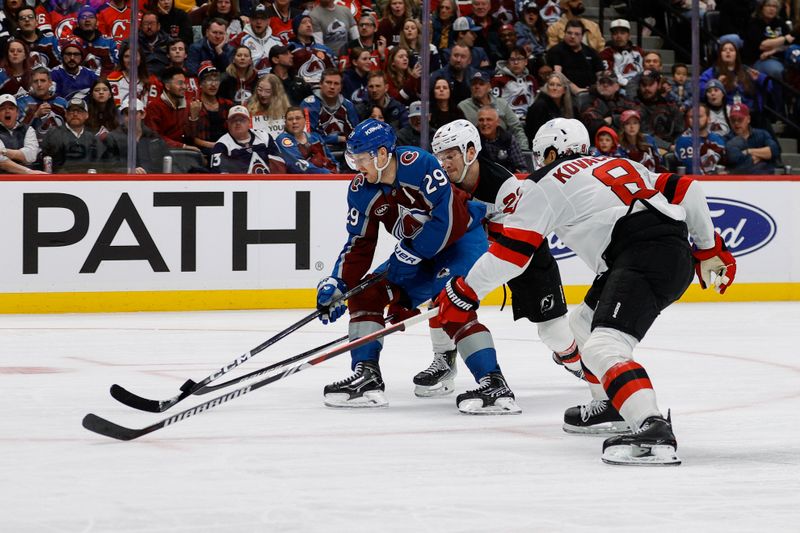 Feb 26, 2025; Denver, Colorado, USA; Colorado Avalanche center Nathan MacKinnon (29) controls the puck under pressure from New Jersey Devils defenseman Brett Pesce (22) and defenseman Johnathan Kovacevic (8) in the second period at Ball Arena. Mandatory Credit: Isaiah J. Downing-Imagn Images