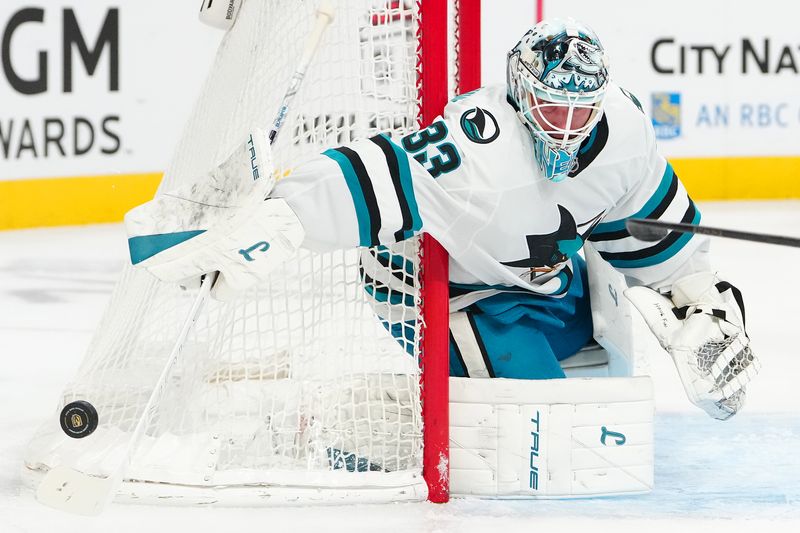 Nov 29, 2025; Las Vegas, Nevada, USA; San Jose Sharks goaltender Alex Nedeljkovic (33) sticks away a Vegas Golden Knights shot during the first period at T-Mobile Arena. Mandatory Credit: Stephen R. Sylvanie-Imagn Images