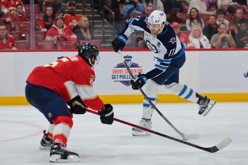 Jan 31, 2026; Sunrise, Florida, USA; Winnipeg Jets center Adam Lowry (17) shoots the puck as Florida Panthers defenseman Aaron Ekblad (5) defends during the first period at Amerant Bank Arena. Mandatory Credit: Sam Navarro-Imagn Images