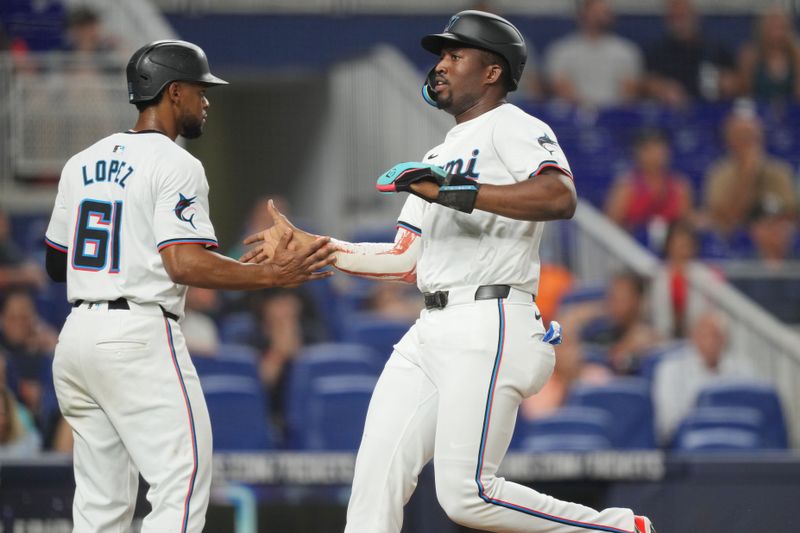 Aug 6, 2024; Miami, Florida, USA;  Miami Marlins designated hitter Jesús Sánchez (12) crosses the plate and is congratulated by Miami Marlins second baseman Otto Lopez (61) in the fourth inning against the Cincinnati Reds at loanDepot Park. Mandatory Credit: Jim Rassol-USA TODAY Sports