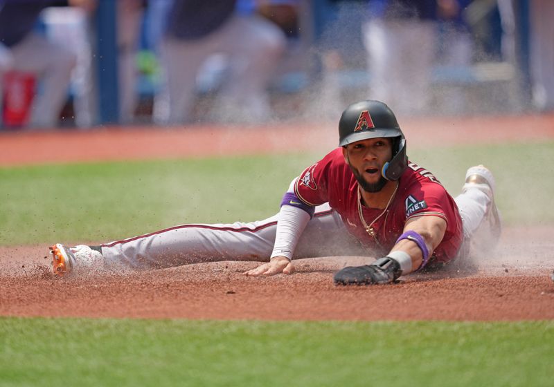 Jul 16, 2023; Toronto, Ontario, CAN; Arizona Diamondbacks left fielder Lourdes Gurriel Jr. (12) slides into home scoring a run against the Toronto Blue Jays during the first inning at Rogers Centre. Mandatory Credit: Nick Turchiaro-USA TODAY Sports