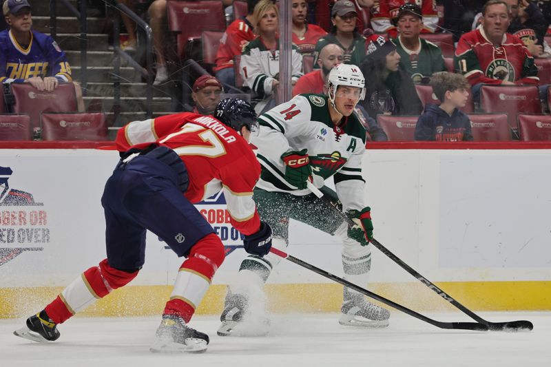 Oct 22, 2024; Sunrise, Florida, USA; Minnesota Wild center Joel Eriksson Ek (14) moves the puck as Florida Panthers defenseman Niko Mikkola (77) defends during the first period at Amerant Bank Arena. Mandatory Credit: Sam Navarro-Imagn Images