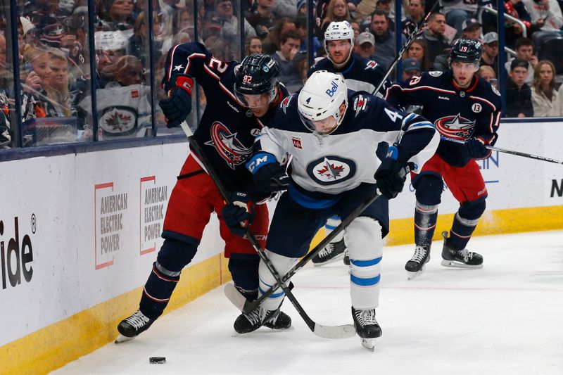 Nov 1, 2024; Columbus, Ohio, USA; Columbus Blue Jackets left wing Mikael Pyyhtia (82) and Winnipeg Jets defenseman Neal Pionk (4) battle for a loose puck  during the second period at Nationwide Arena. Mandatory Credit: Russell LaBounty-Imagn Images