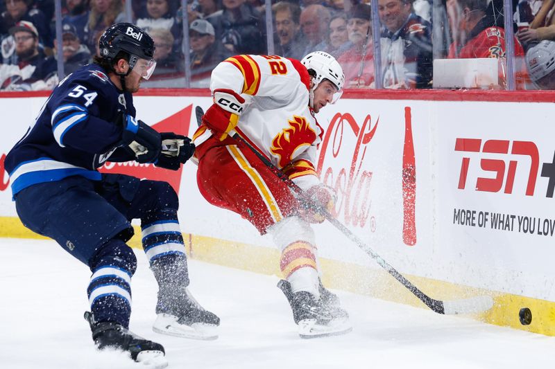 Jan 26, 2025; Winnipeg, Manitoba, CAN;  Winnipeg Jets defenseman Dylan Samberg (54) and Calgary Flames forward Jacob Pelletier (22) contest for the puck during the first period at Canada Life Centre. Mandatory Credit: Terrence Lee-Imagn Images